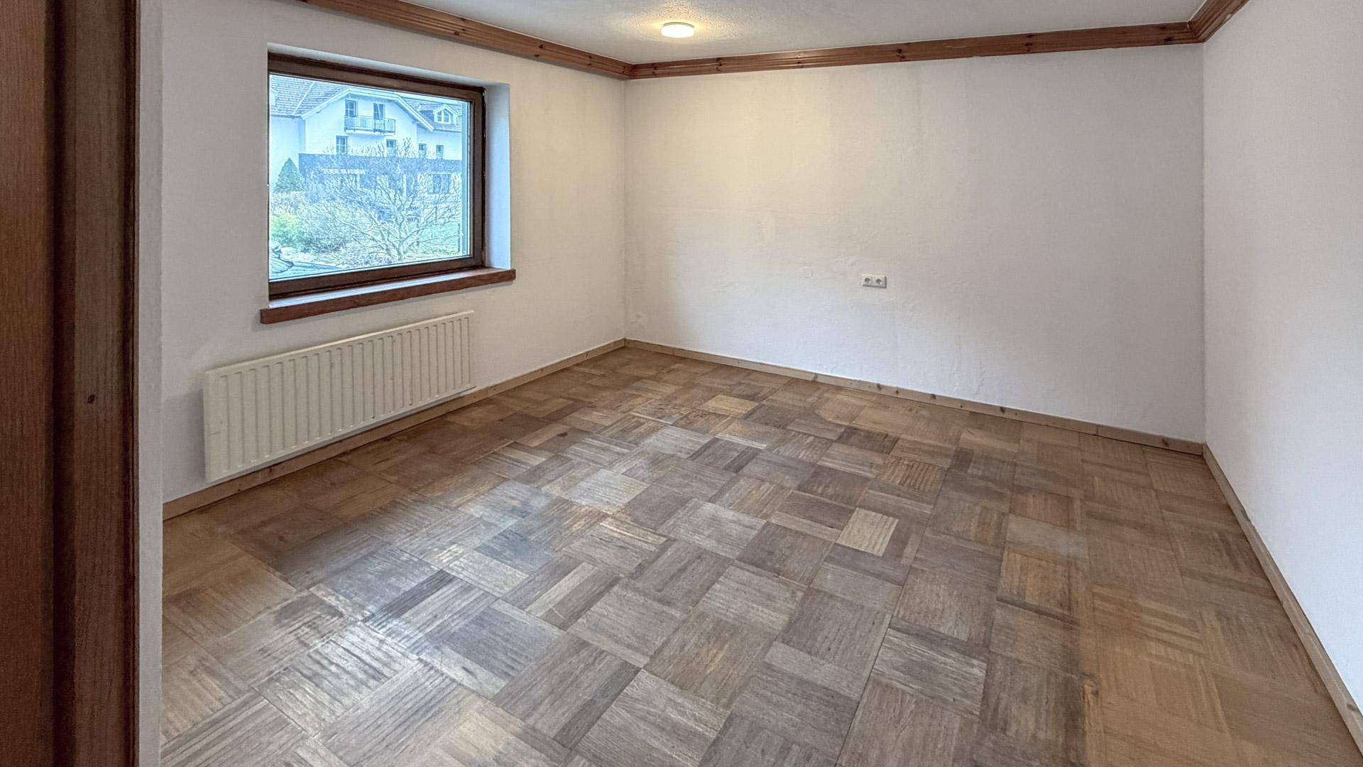 Geräumiges Schlafzimmer mit Parkettboden, weißen Wänden und Holzdeckenbalken.