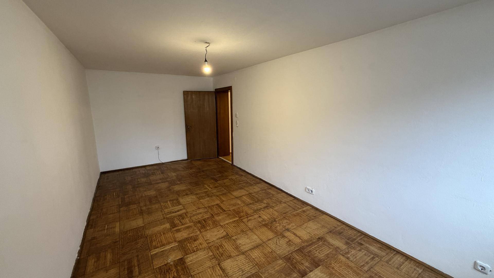 Leeres Zimmer mit Parkettboden und einfacher Deckenleuchte, bereit zur Einrichtung.