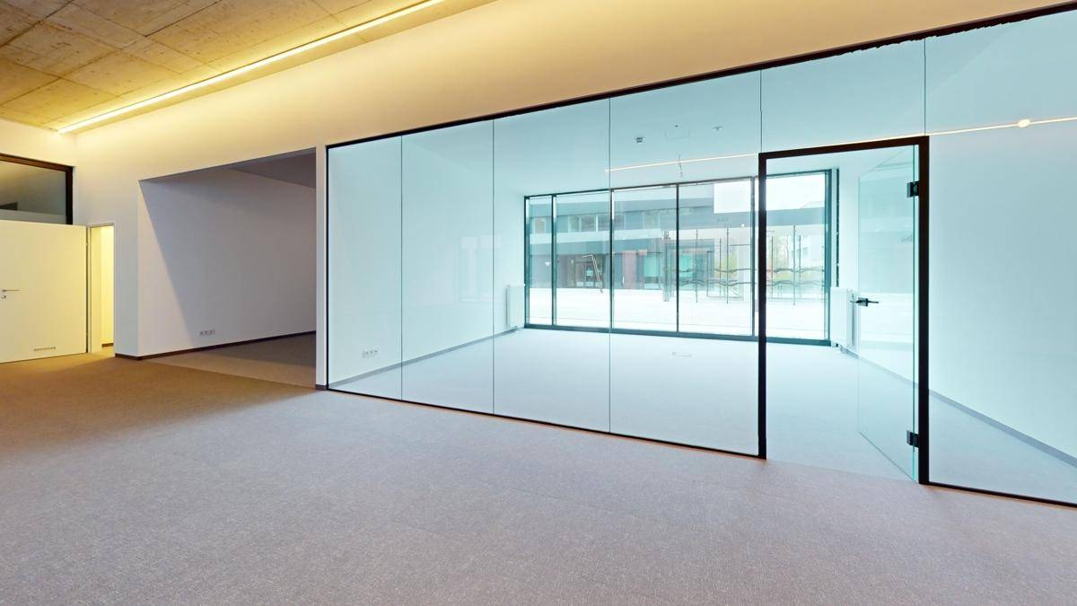 Einzelbüro mit Glaswänden und großen Fenstern, die viel Tageslicht hereinlassen und einen Blick nach draußen bieten.