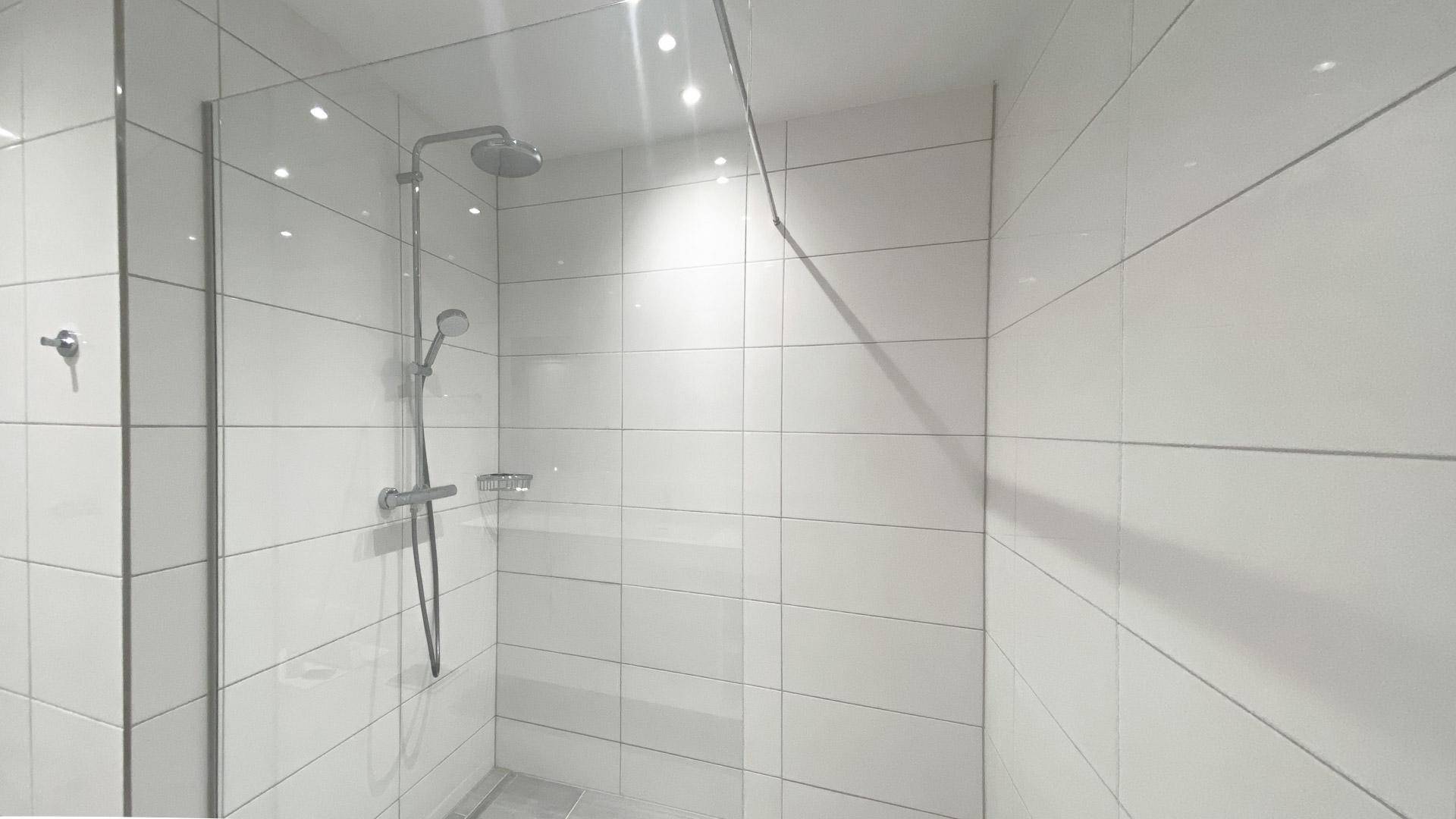 Geräumige, moderne Duschkabine mit Regendusche und Glasabtrennung in einem gefliesten Bad.