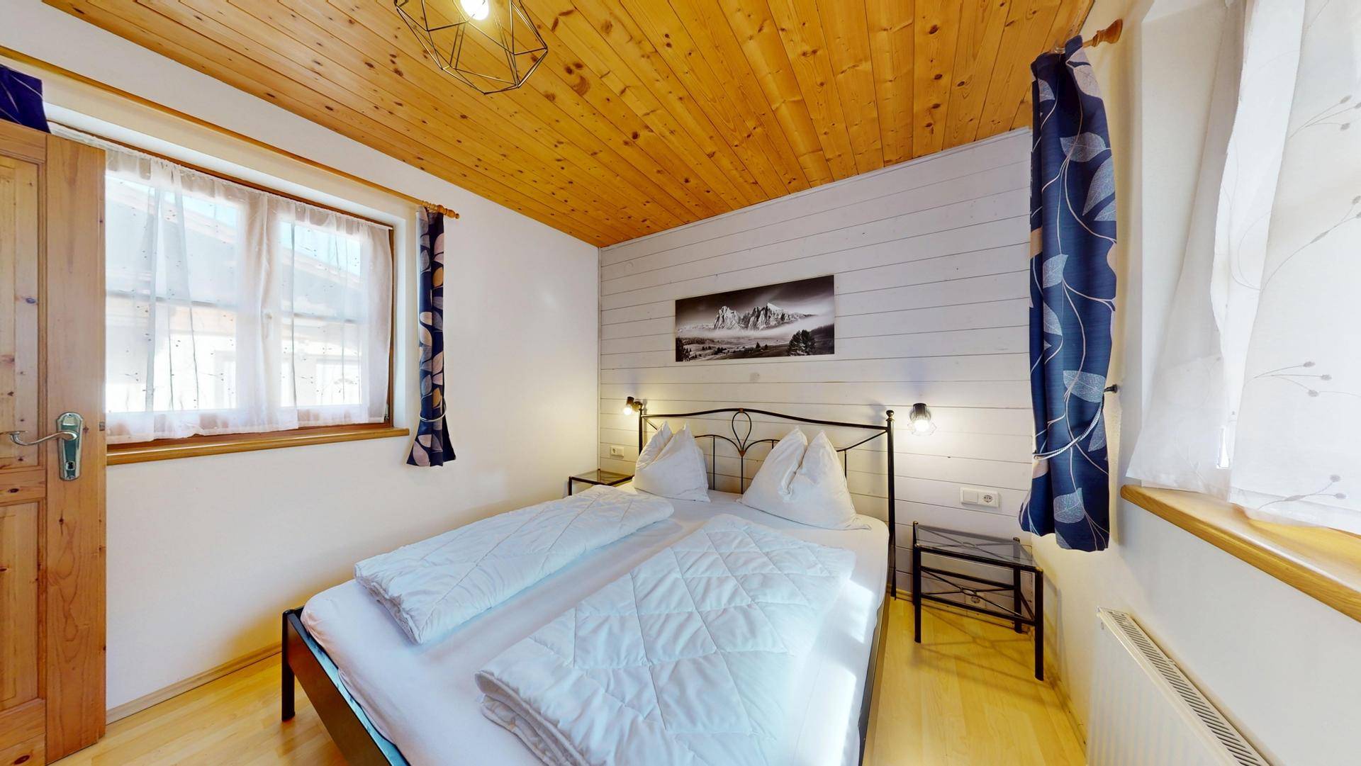 Helles Schlafzimmer mit Doppelbett, Nachttischen und einem Bild an der weiß getäfelten Wand.
