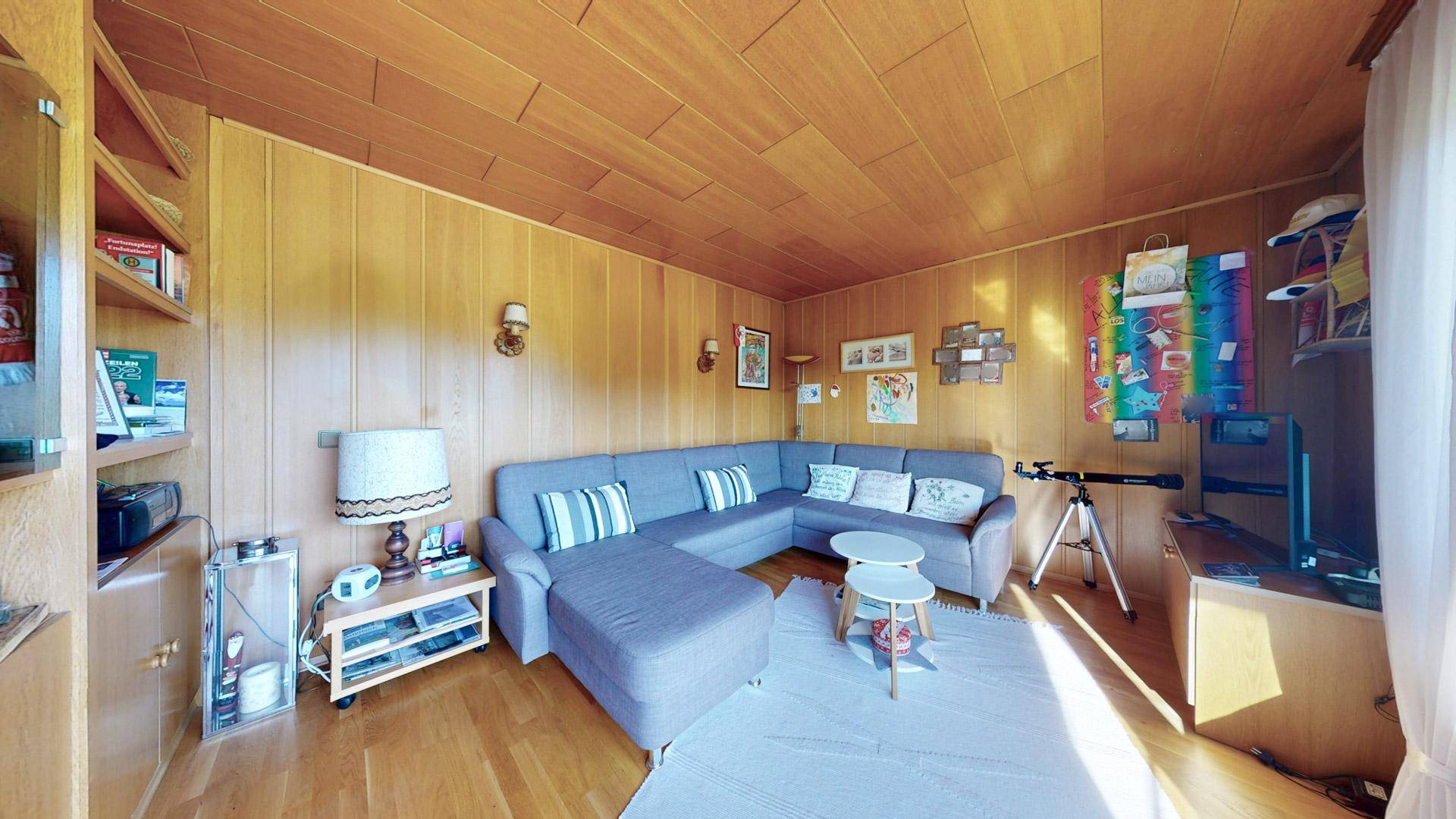 Wohnzimmer mit Holzvertäfelung, bequemer Sitzecke und Regalen für Stauraum.