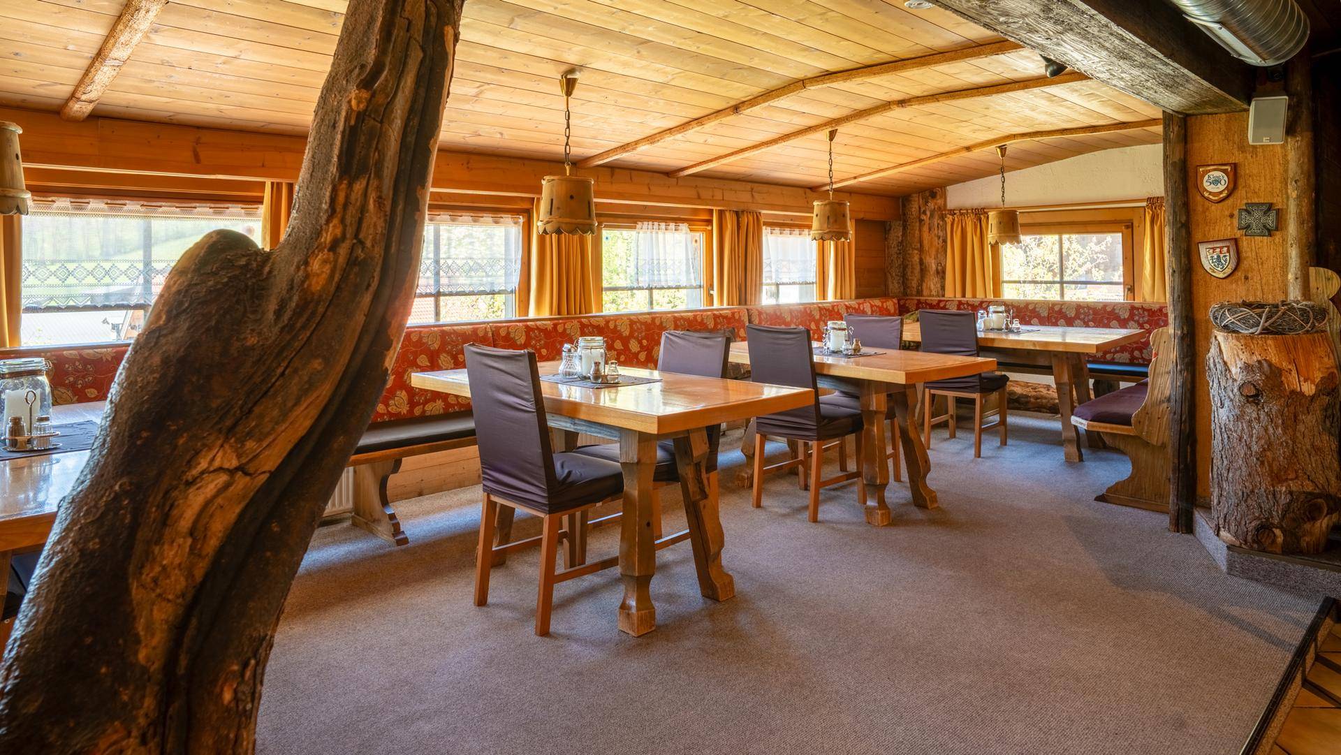 Geräumiger Speisesaal im alpinen Stil mit Holzbalkendecke und großen Fenstern.