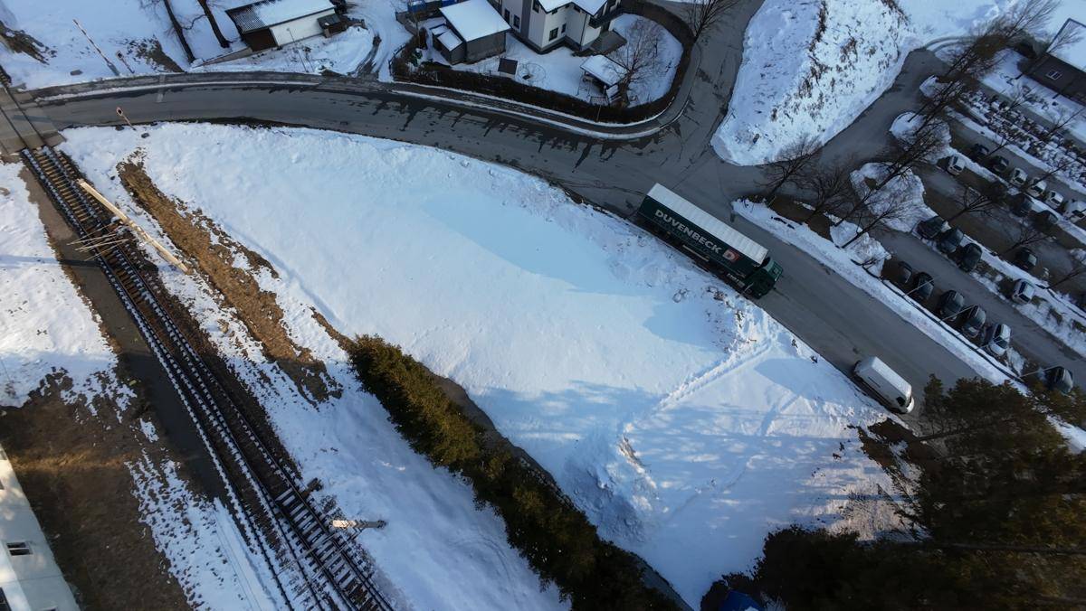 Luftaufnahme einer verschneiten Landschaft mit Straße, Bahngleisen und einem Lastwagen, umgeben von Bäumen.