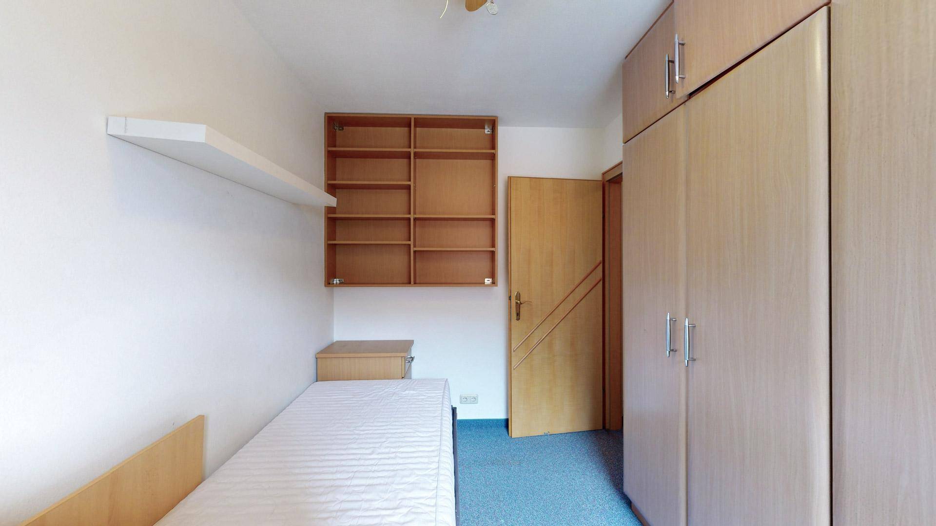 Schlafzimmer mit Einzelbett, Wandregalen und einem großen Kleiderschrank.