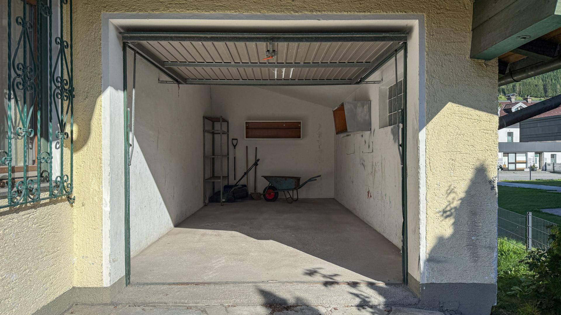 Leere Garage mit Betonboden, Regalen und Gartengeräten, bereit zur Nutzung als Abstellraum.