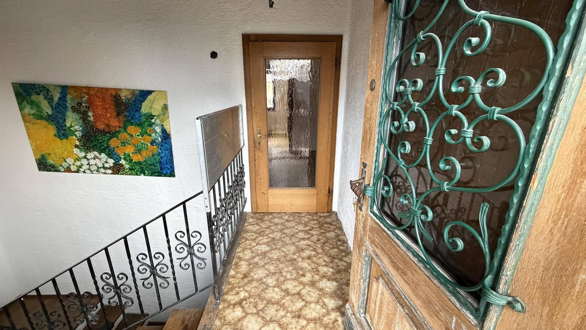 Eingangsbereich mit verzierter Eisentür, Treppe und gemustertem Fliesenboden.