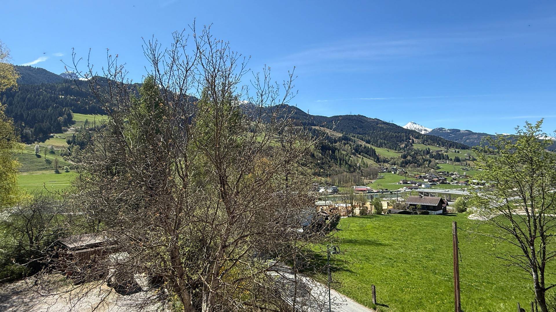 Panoramablick auf die grüne Berglandschaft mit vereinzelten Häusern unter blauem Himmel.