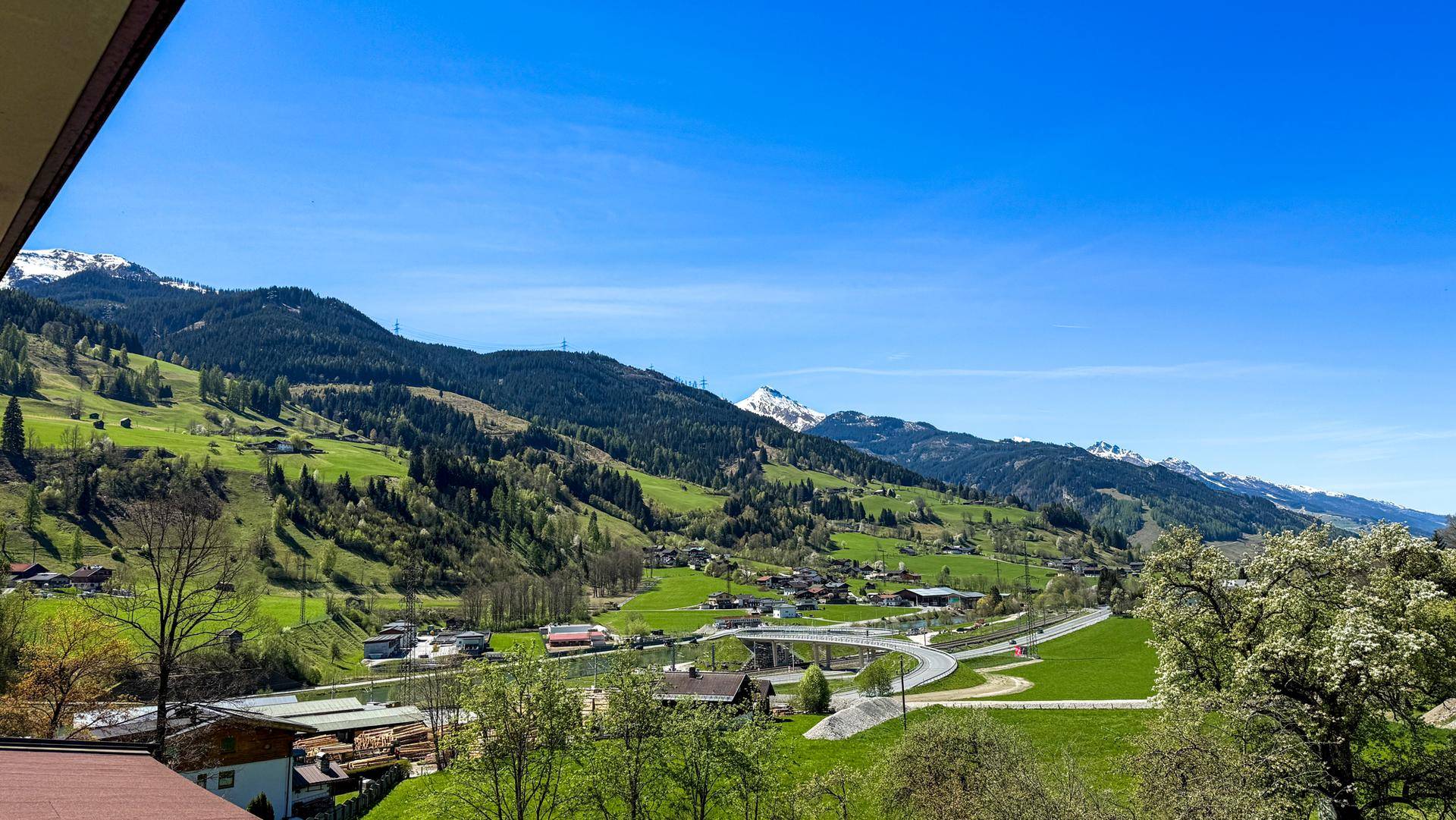 Breiter Panoramablick auf die grüne Alpenlandschaft mit Bergen und Tälern unter blauem Himmel.
