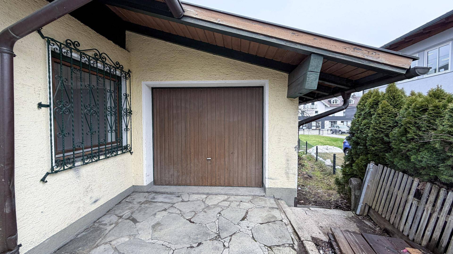 Einzelgarage mit braunem Holztor und gepflastertem Vorplatz am Haus.