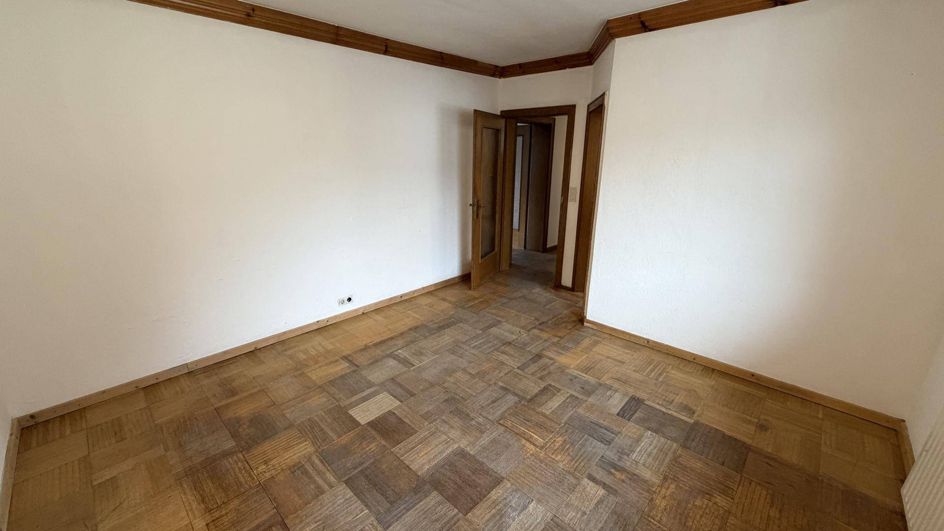 Geräumiges Zimmer mit Parkettboden und Holztürrahmen, ideal für Wohnzwecke.