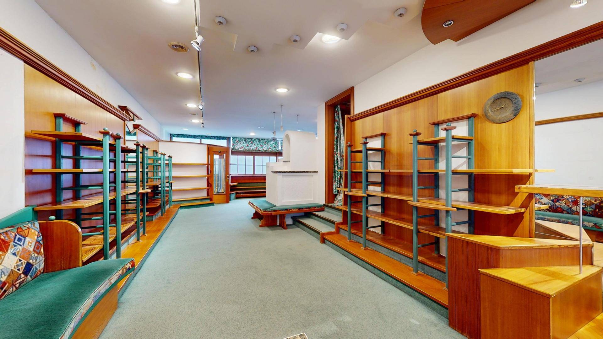 Langer Verkaufsraum mit Regalen, Teppichboden und einem zentralen Präsentationselement.
