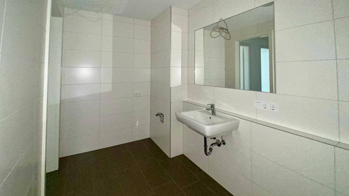 Helles Badezimmer mit Waschbecken und großen weißen Wandfliesen, bereit für die Installation einer Dusche.