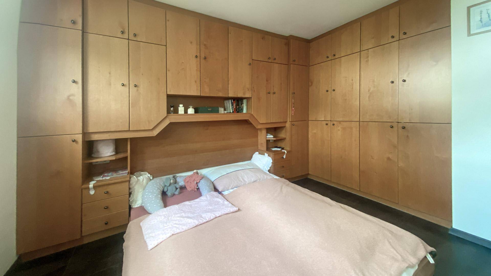 Schlafzimmer mit großem Einbauschrank aus Holz und Doppelbett.