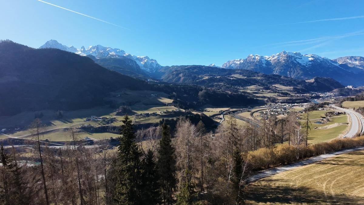 Panoramablick über ein weites Tal mit schneebedeckten Bergen, einer Stadt und einer Autobahn.
