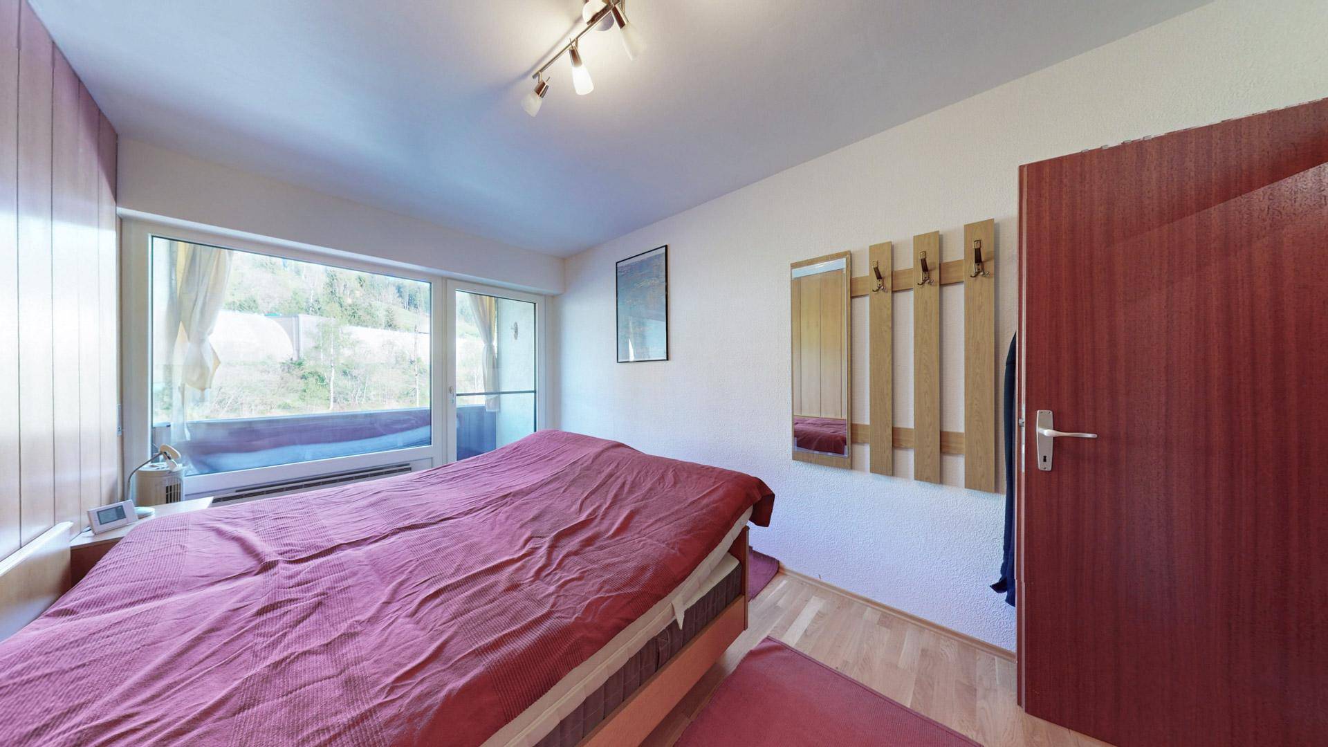 Helles Schlafzimmer mit Holzboden, Doppelbett und Fensterfront zum Balkon.