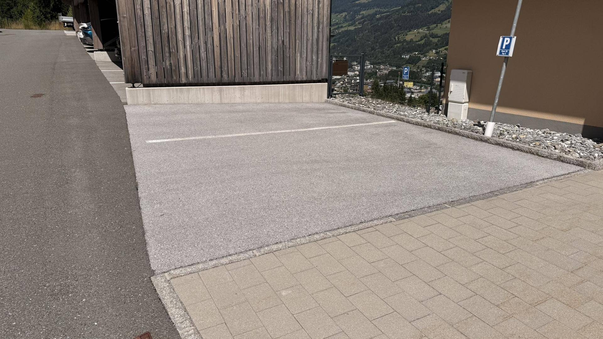 Detailansicht des Parkplatzes neben einem Gebäude mit Holzverkleidung und Bergpanorama im Hintergrund.