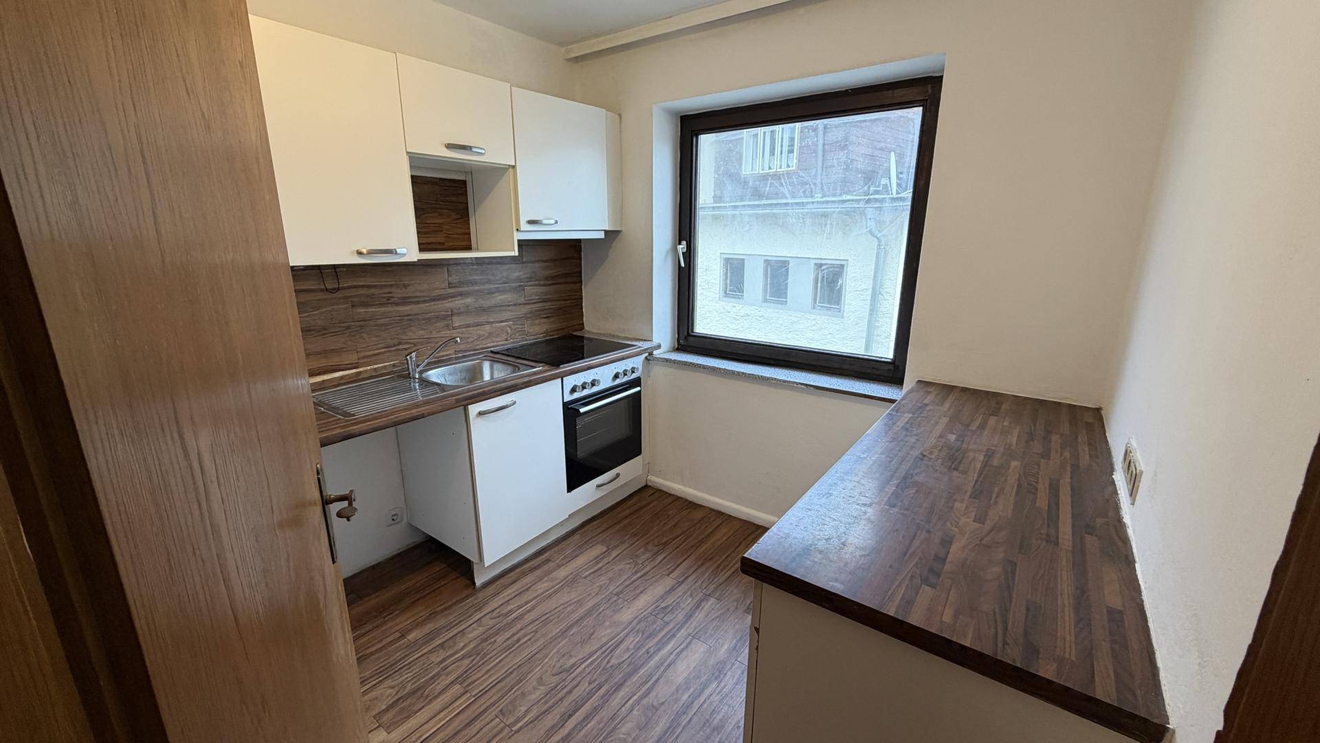 Kleine Küche mit weißen Schränken, Holzarbeitsplatte und Fenster.