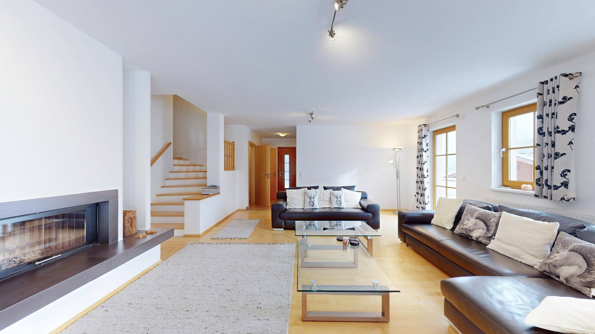 Geräumiges Wohnzimmer mit gemütlicher Sitzecke, Kamin und hellen Holzfenstern.