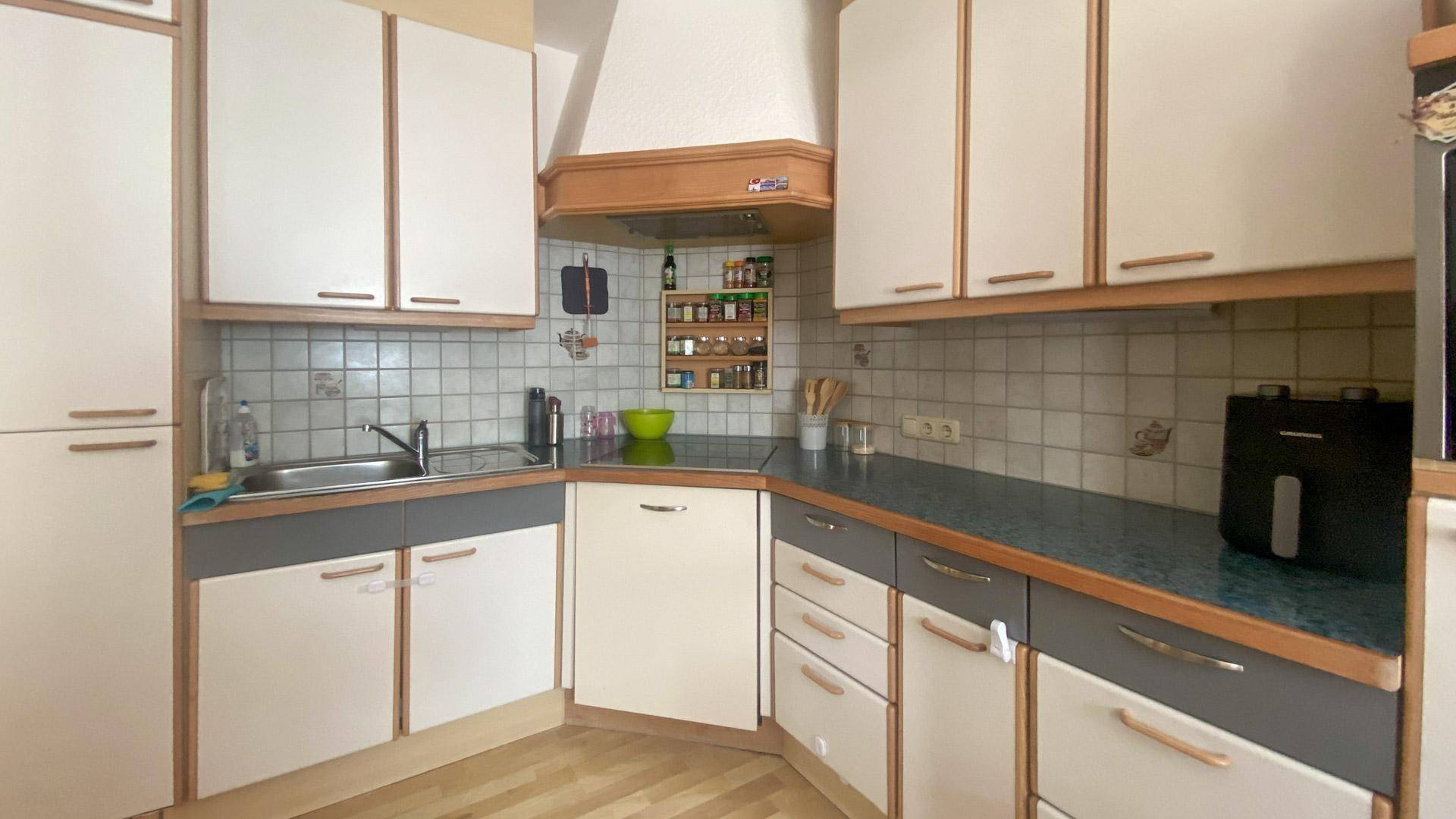 Küche mit hellen Holz- und weißen Schränken, dunkler Arbeitsplatte und Fliesenrückwand.