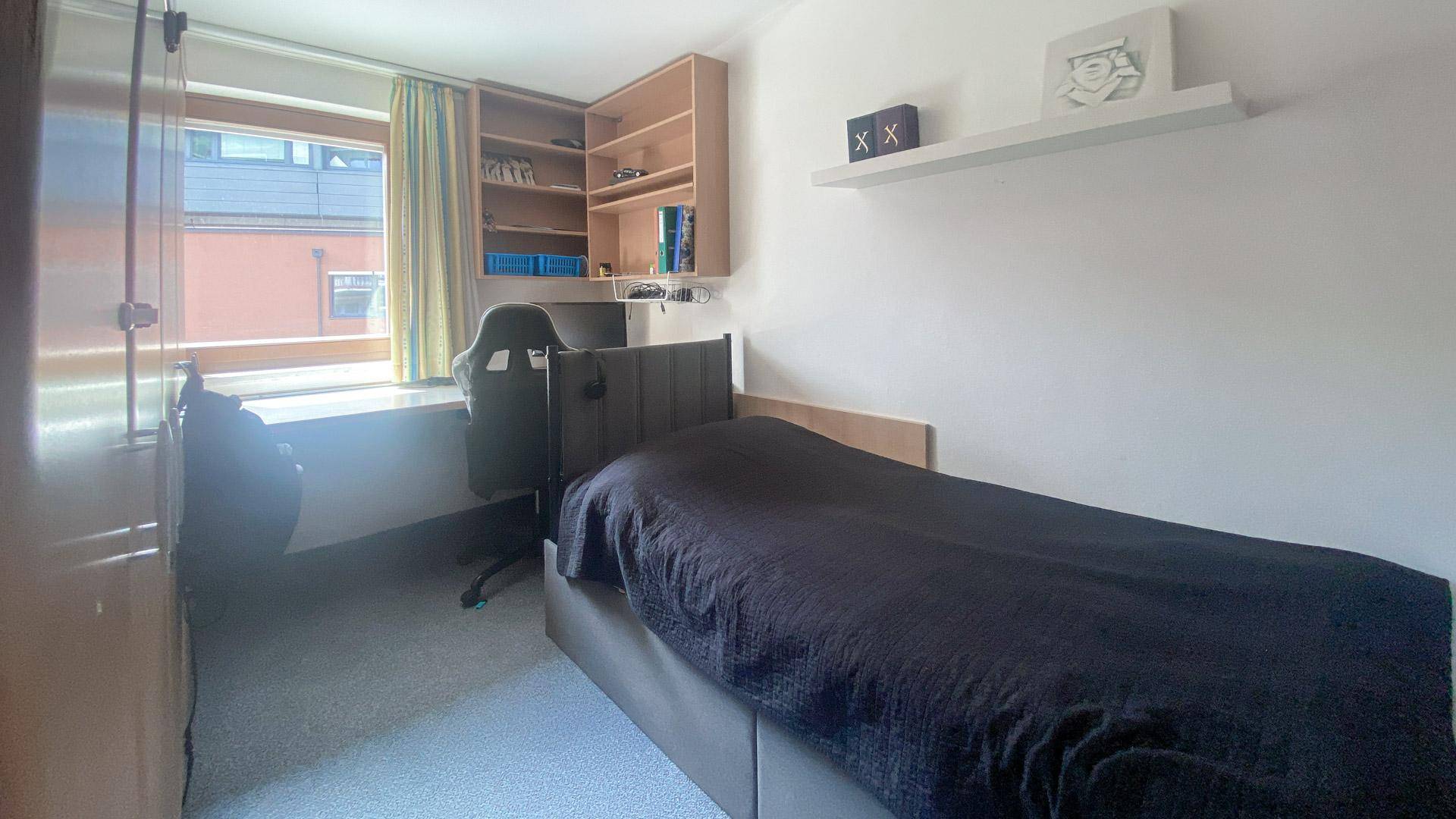 Helles Schlafzimmer mit Einzelbett, Schreibtisch und Fensterblick.