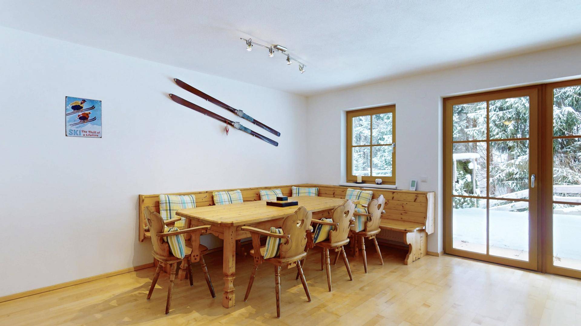 Traditioneller Essbereich mit Holztisch, Eckbank und großen Fenstern mit Blick auf die verschneite Landschaft.