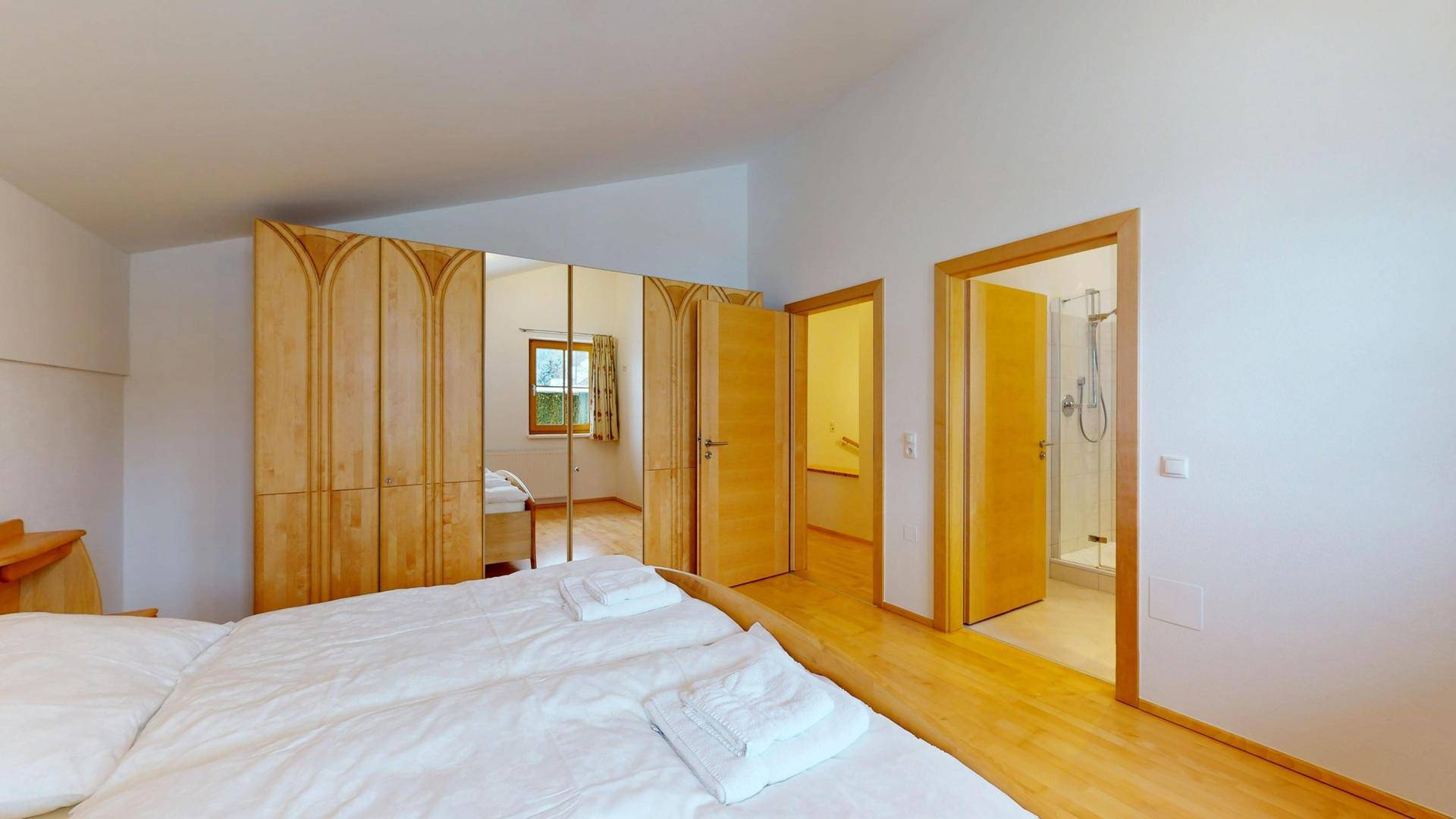 Schlafzimmer mit Holzboden und Zugang zu einem modernen Badezimmer mit Dusche.