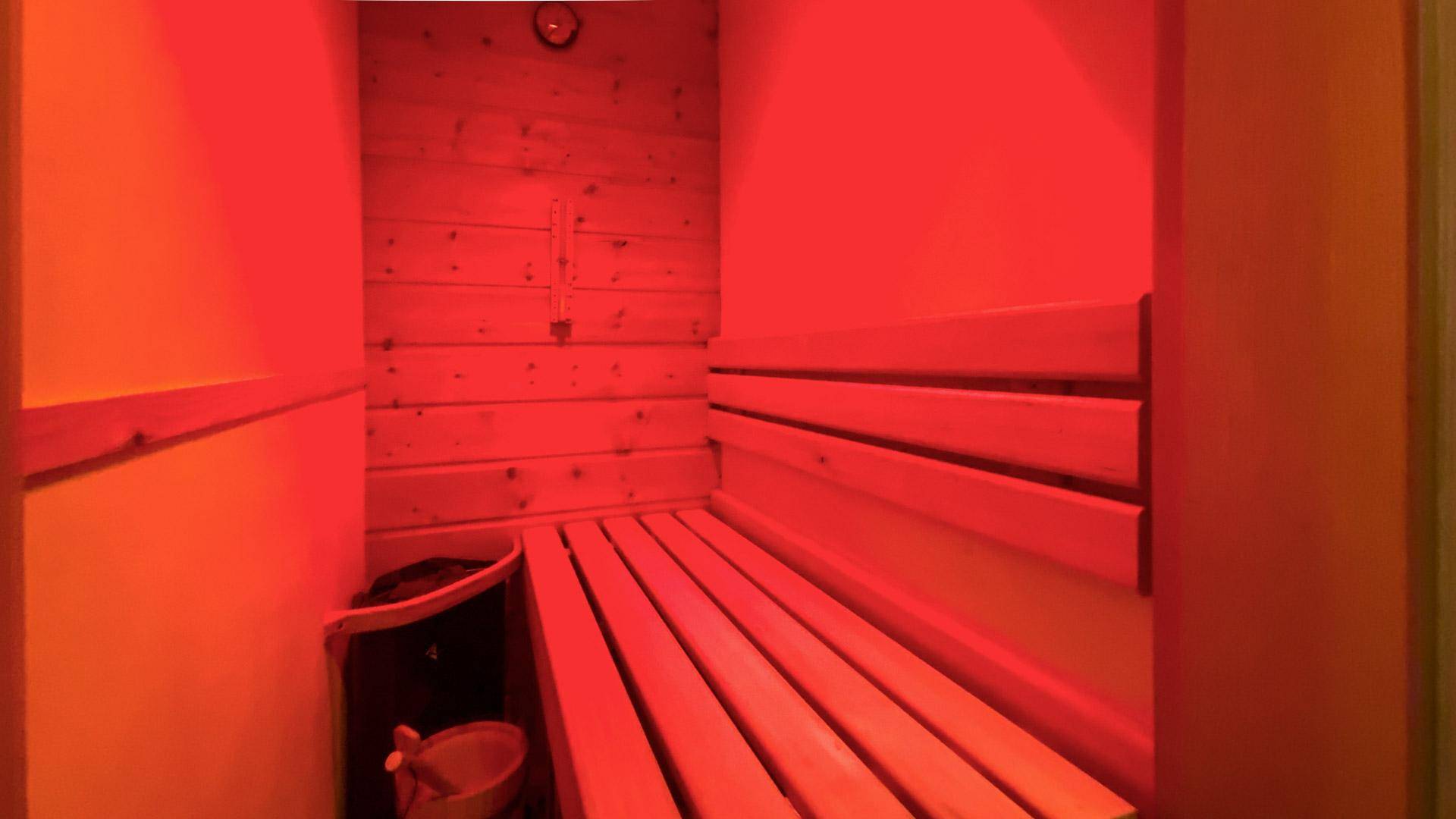 Gemütliche Sauna mit Holzverkleidung und Bänken, beleuchtet in warmem Rotlicht.