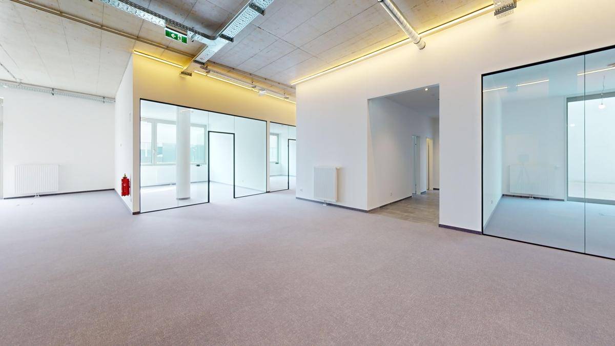 Geräumiger Bürobereich mit Teppichboden, Glasabtrennungen und sichtbaren Installationen an der Decke.