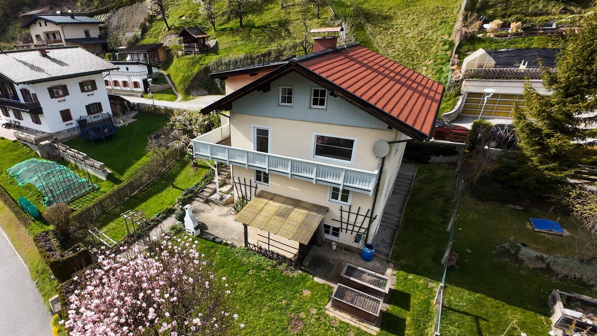 Luftaufnahme des Hauses mit rotem Dach, Balkon und großem Garten in Hanglage.