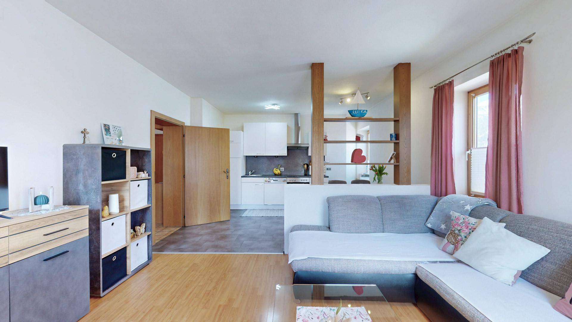 Offener Wohnbereich mit Sofa und Blick in die moderne Küche sowie den angrenzenden Flur.