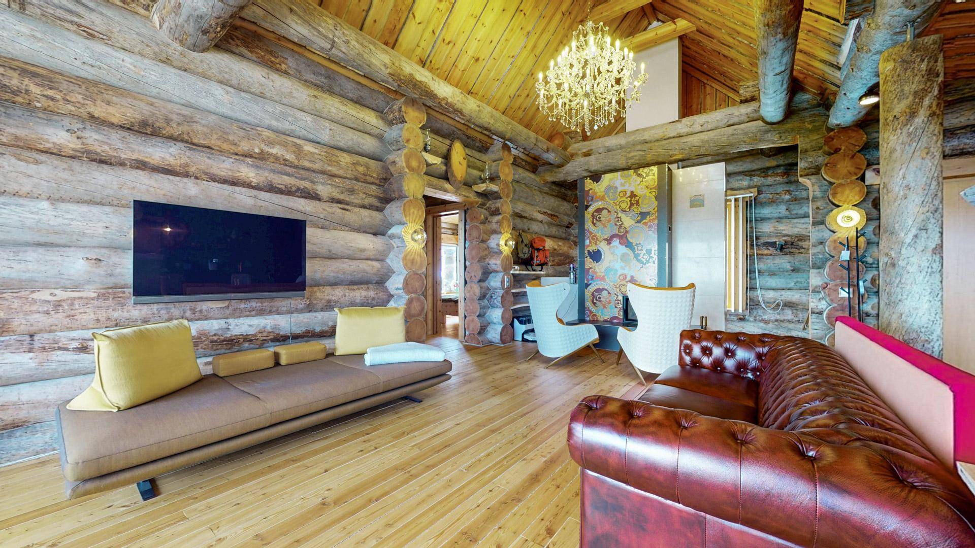 Gemütliches Wohnzimmer mit Holzwänden, bequemen Sofas und einem eleganten Kronleuchter.