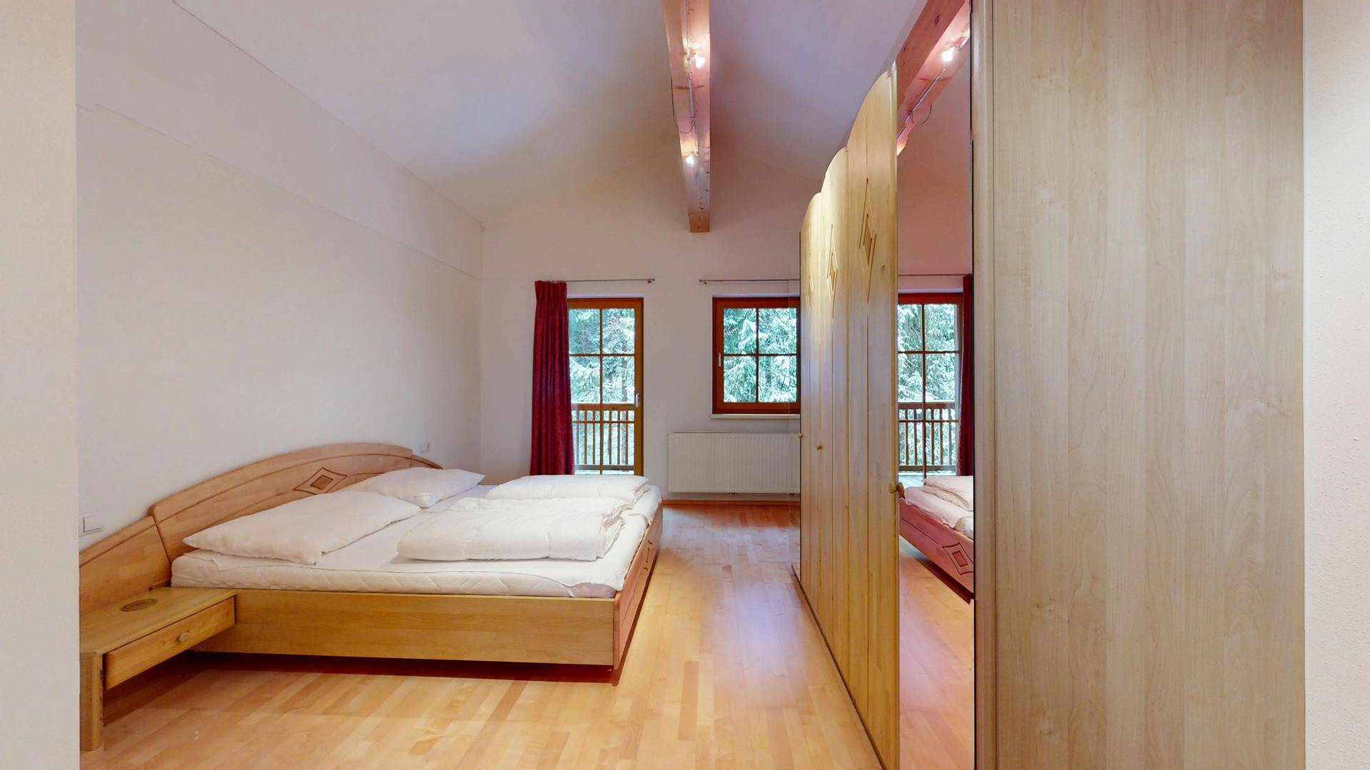 Gemütliches Schlafzimmer mit Doppelbett, sichtbaren Holzbalken und Balkonzugang.