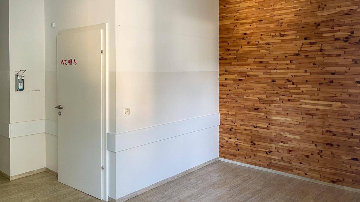 Flur mit dekorativer Holzwandverkleidung und einer Tür, die zu den Toiletten führt.