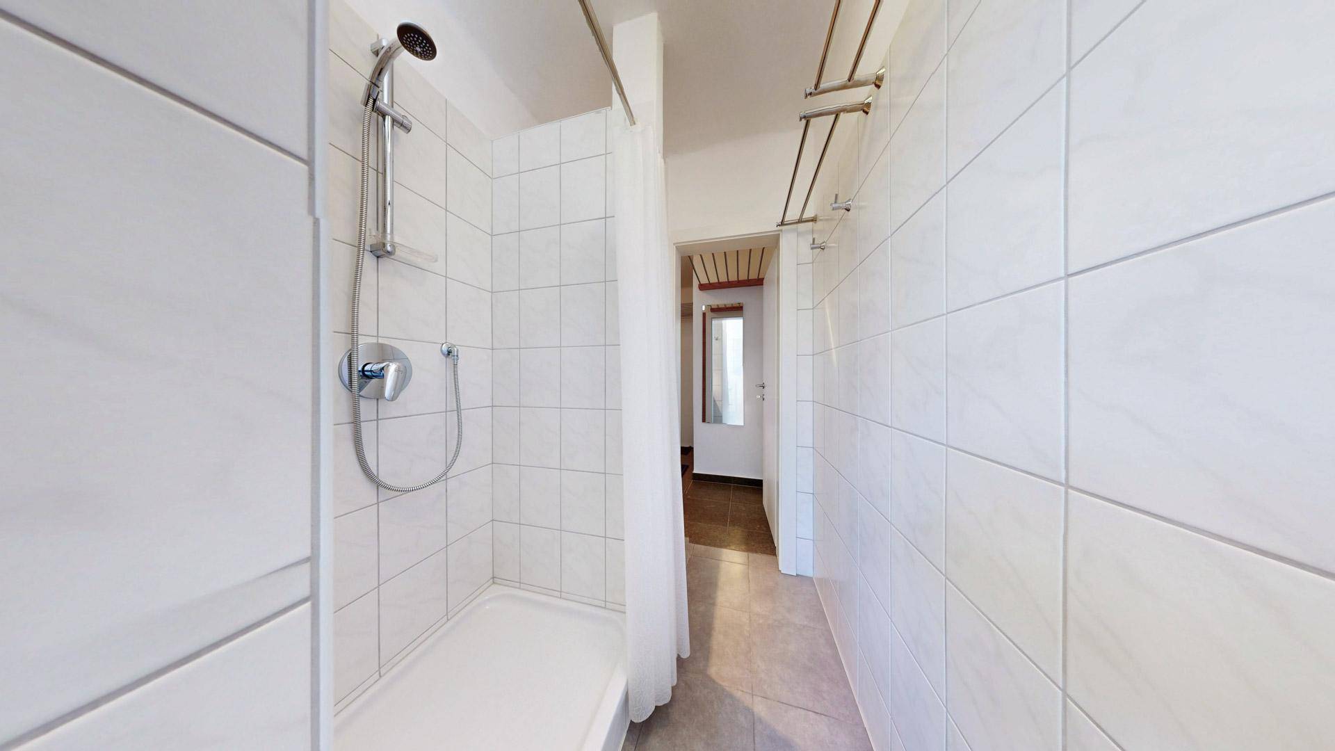Heller Duschbereich im Badezimmer mit weißen Fliesen und einfacher Duschvorrichtung.