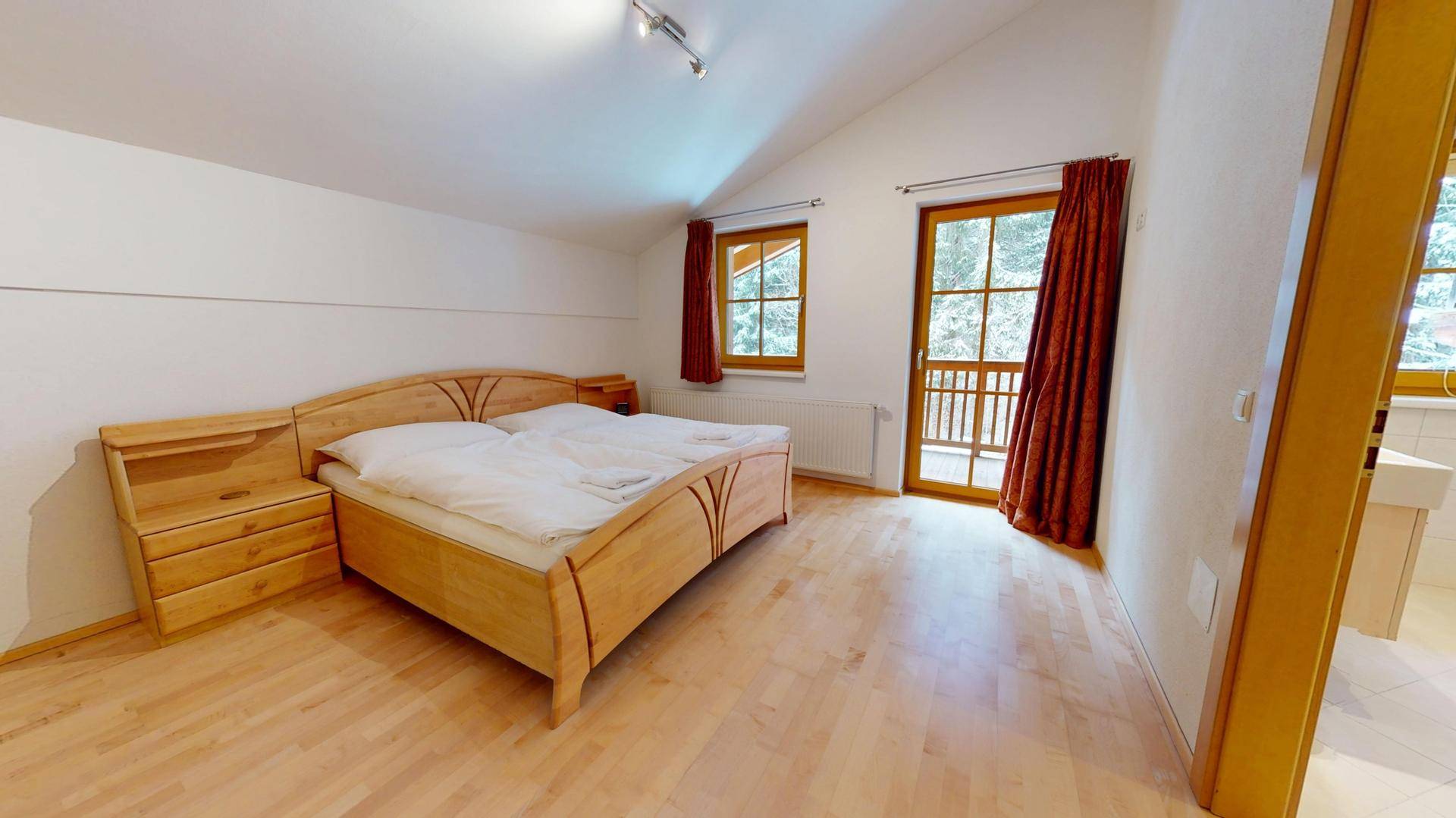 Helles Schlafzimmer mit Holzbett, Parkettboden und Zugang zu einem französischen Balkon.