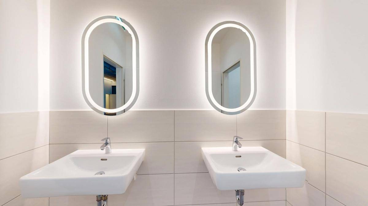 Modernes Badezimmer mit zwei beleuchteten Spiegeln und zwei Waschbecken, ideal für mehrere Nutzer.