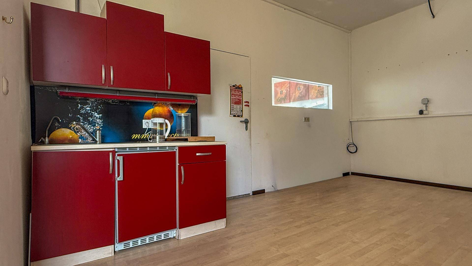 Kleine Küchenzeile mit roten Schränken und einem integrierten Kühlschrank in einem hellen Raum.