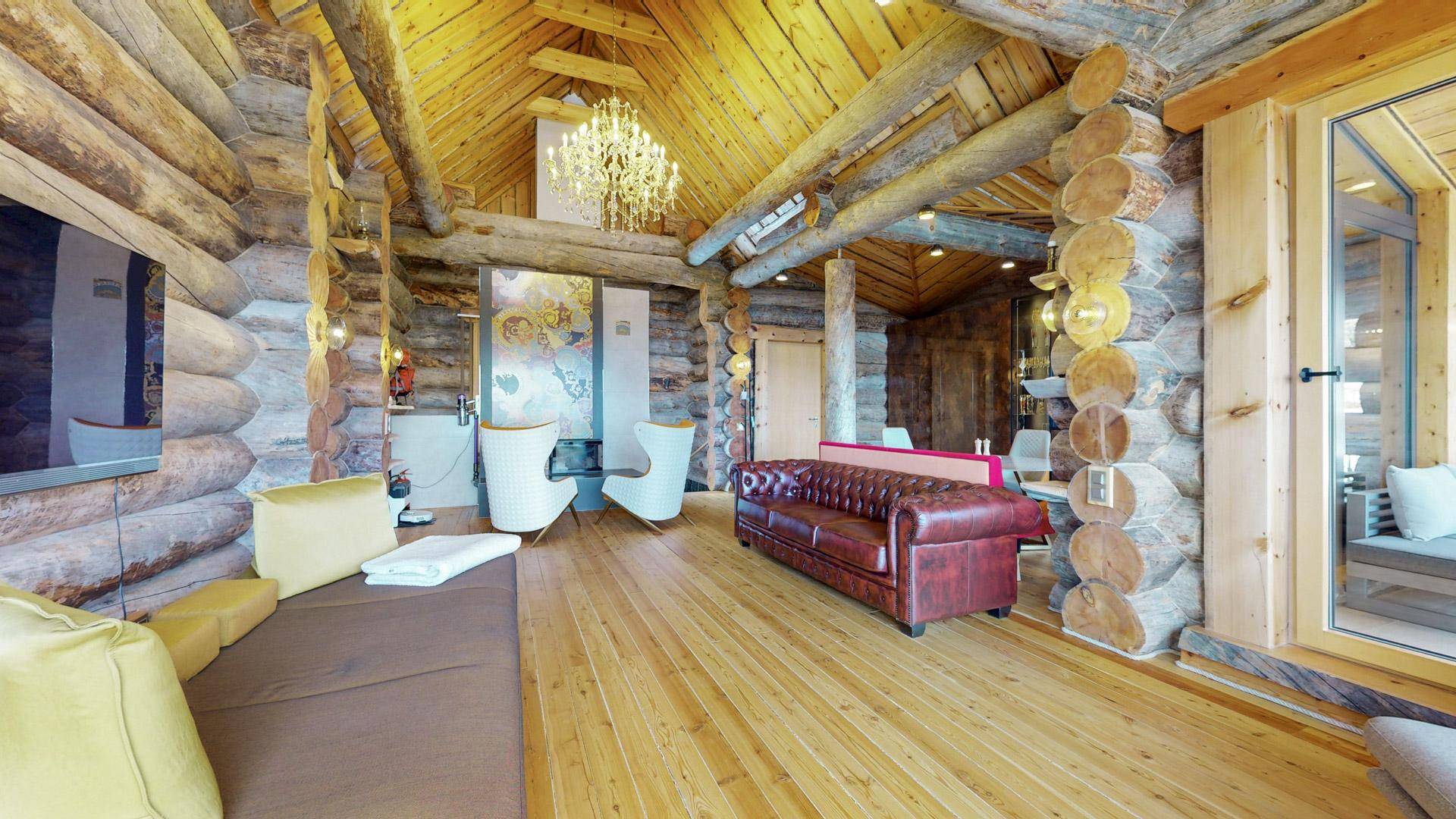 Geräumiges Wohnzimmer im Chalet-Stil mit Holzbalken, Kronleuchter und gemütlichen Sitzgelegenheiten.