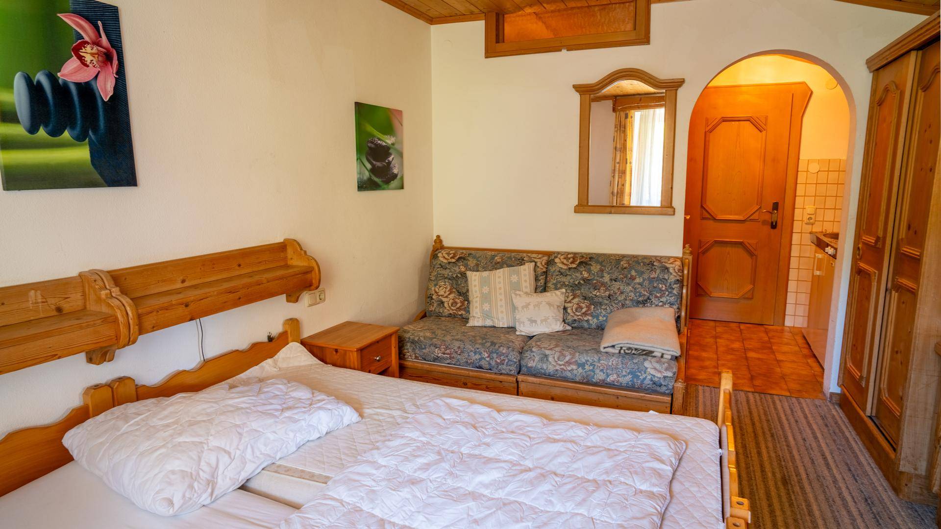 Rustikales Schlafzimmer mit Holzdoppelbett, Sofa und Zugang zu einem kleinen Bad.