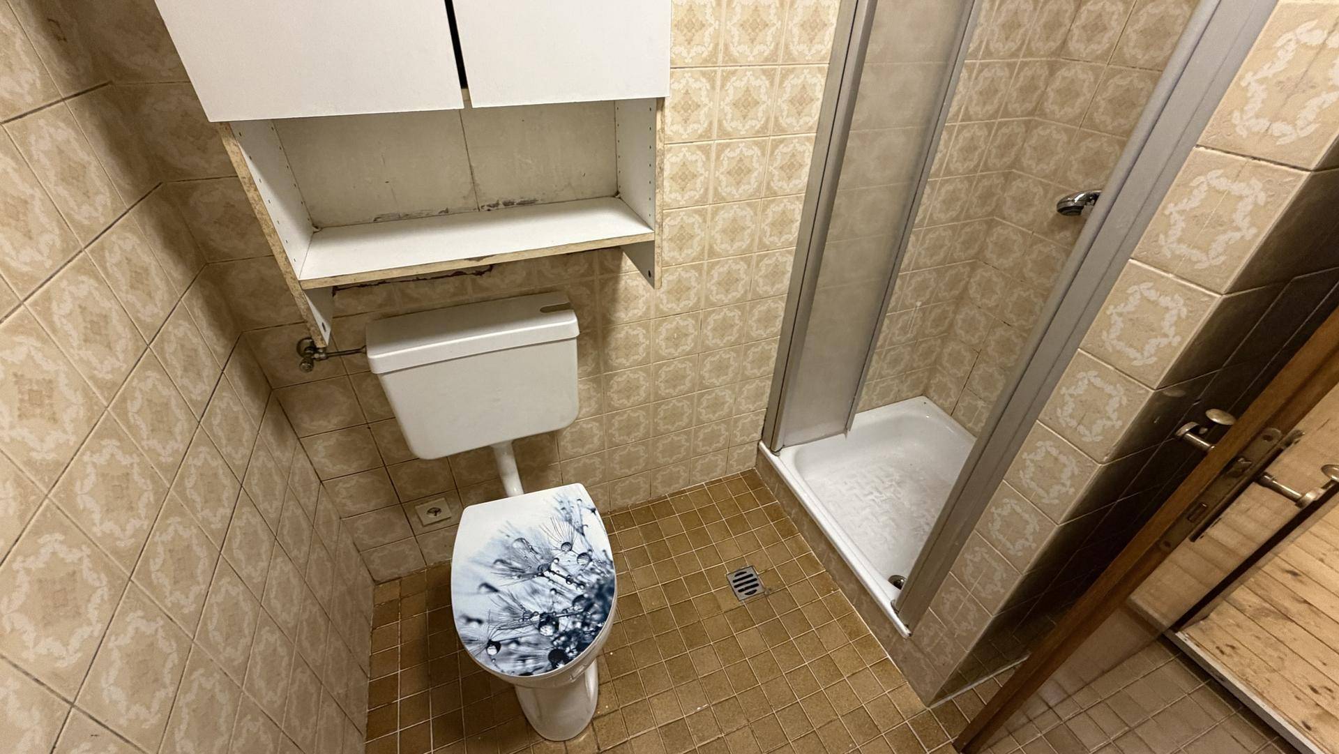 Badezimmer mit Dusche, Toilette und gemusterten Fliesen im Vintage-Stil.