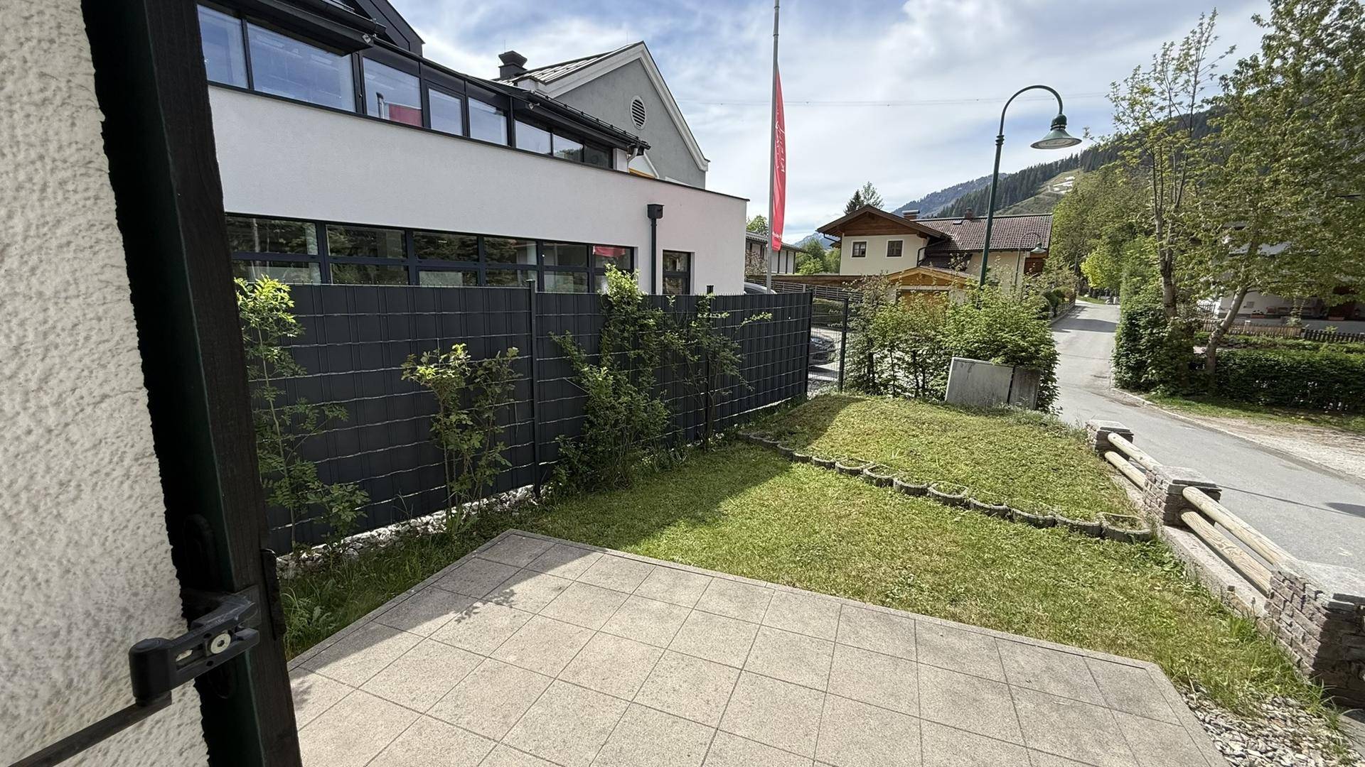 Kleine gepflasterte Terrasse mit Rasenfläche und Blick auf die umliegende Bebauung.