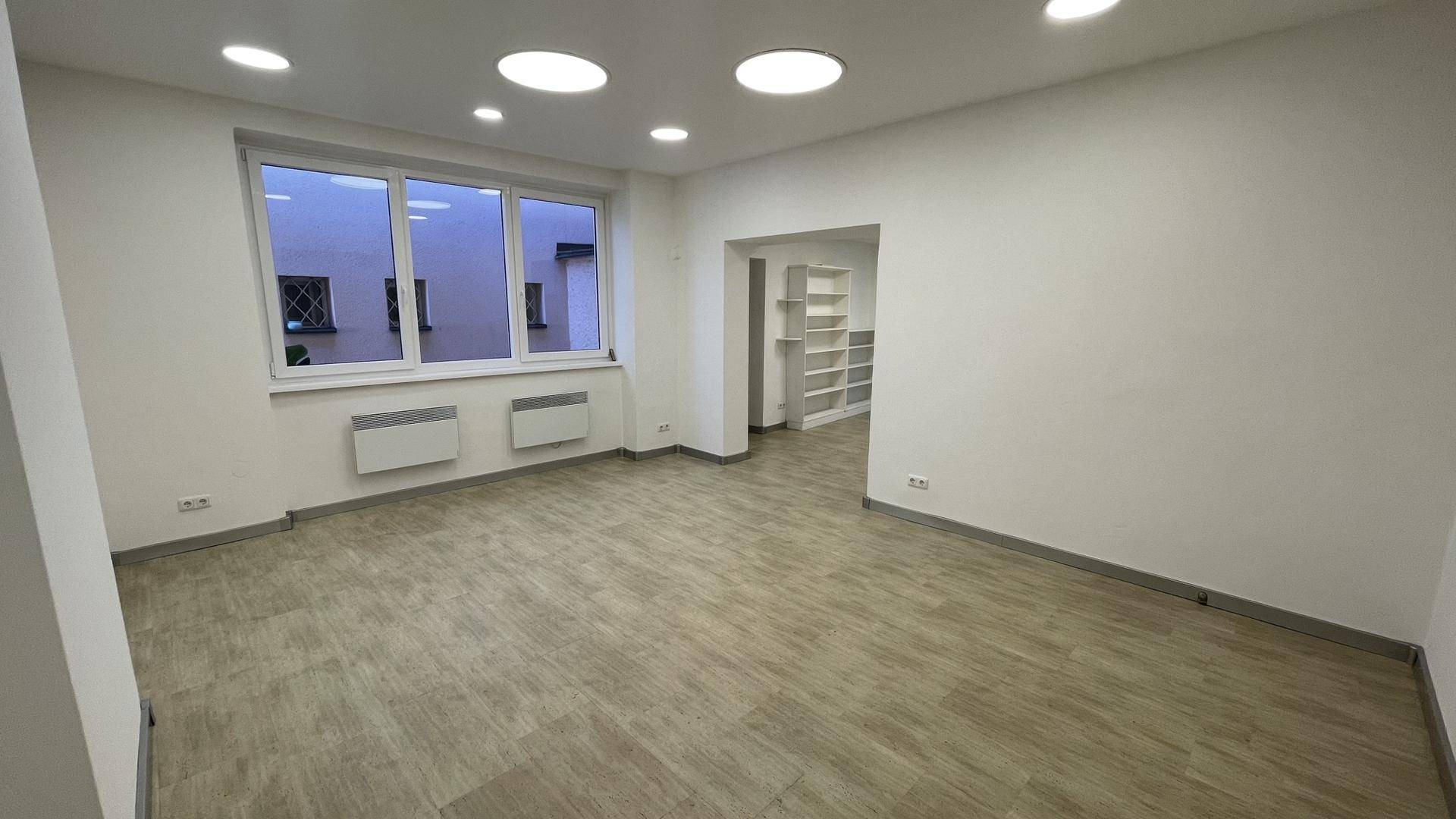 Helles Wohnzimmer mit großen Fenstern, Holzoptikboden, Wandheizkörpern und Deckenstrahlern.