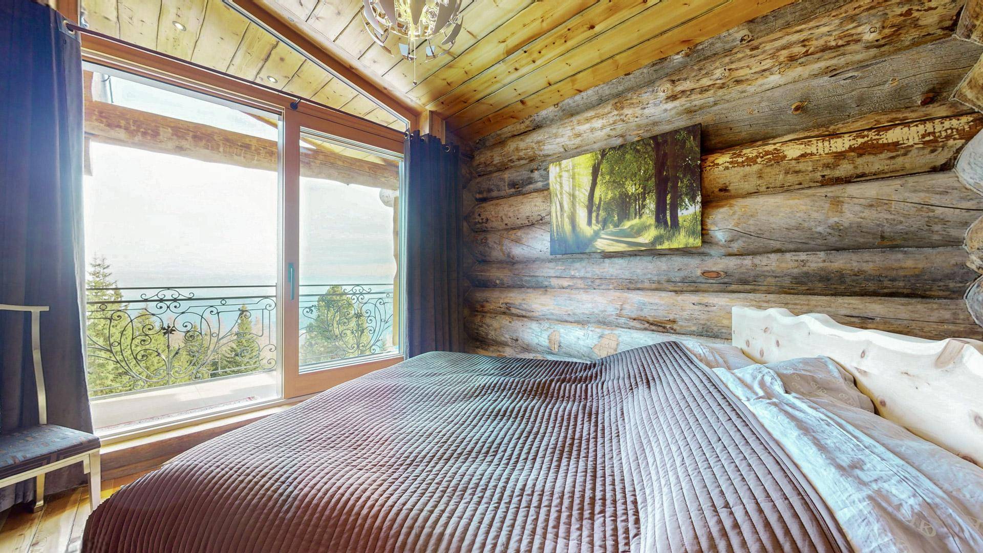 Helles Schlafzimmer mit Holzwänden, großem Fenster und Zugang zu einem Balkon mit Bergblick.