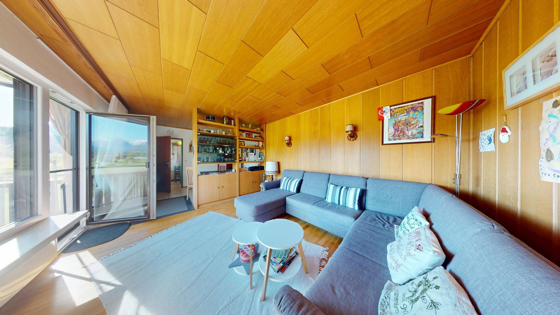 Wohnzimmer mit Ecksofa, Holzvertäfelung und Zugang zum Balkon, der eine schöne Aussicht bietet.