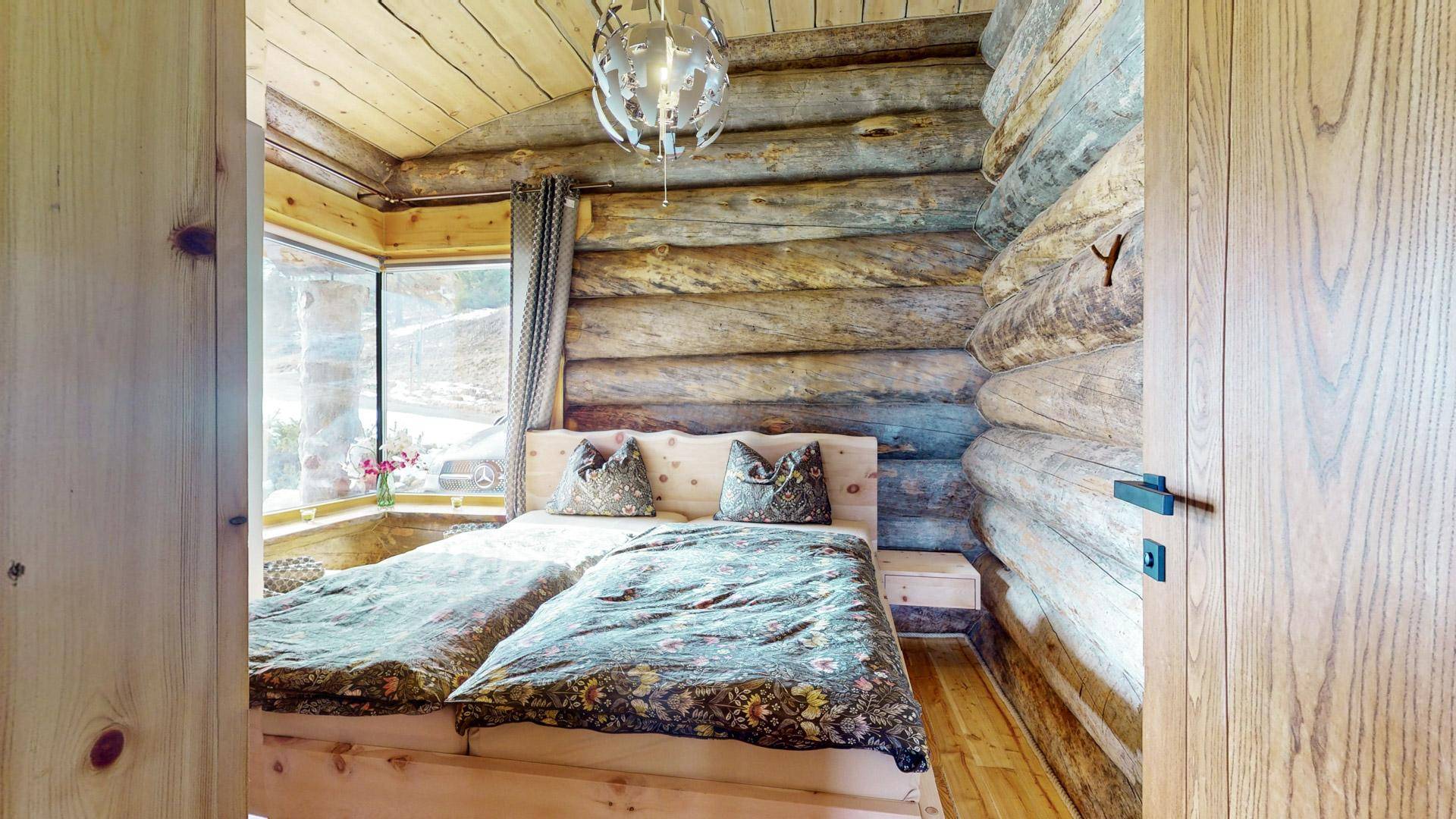 Gemütliches Schlafzimmer mit zwei Einzelbetten, Holzwänden und einem Fenster mit Blick ins Grüne.