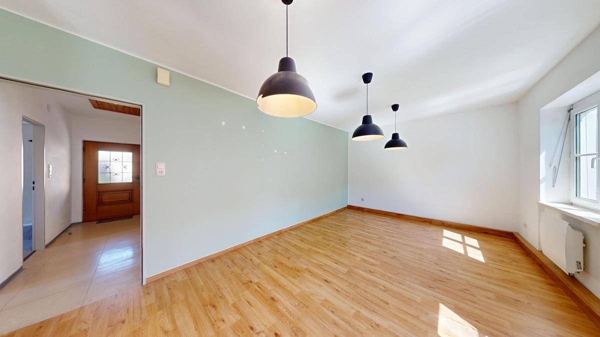 Heller Wohnraum mit Holzboden, einer hellgrünen Akzentwand und Blick auf den Eingangsbereich.