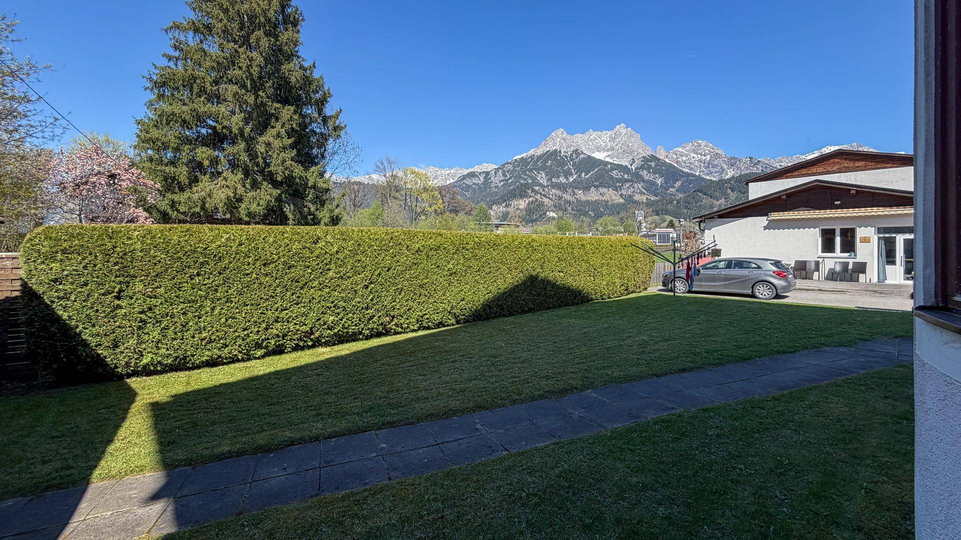 Gepflegter Garten mit Rasenfläche, Hecke und beeindruckendem Bergblick im Hintergrund.