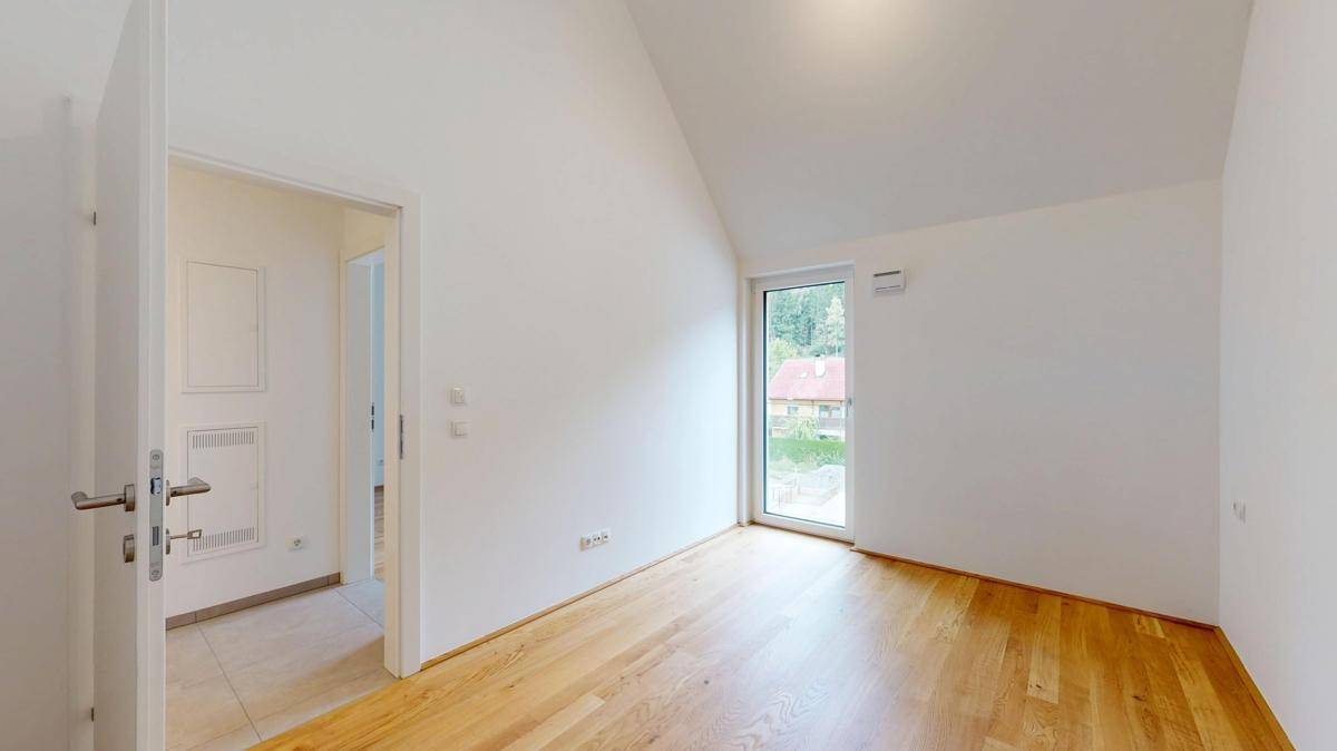 Helles Zimmer mit Holzboden und einem Fenster, das viel Tageslicht hereinlässt.