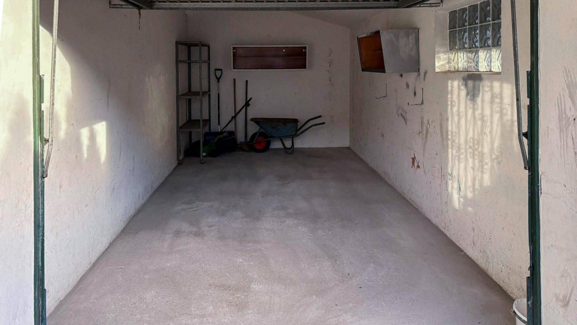 Leere Garage mit Betonboden und Werkzeugen an der Wand.